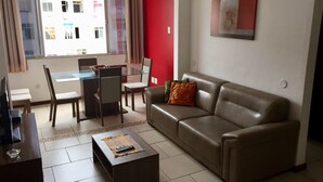 Een woonkamer met een bank, een salontafel, een televisie en een eethoek met stoelen en een tafel.