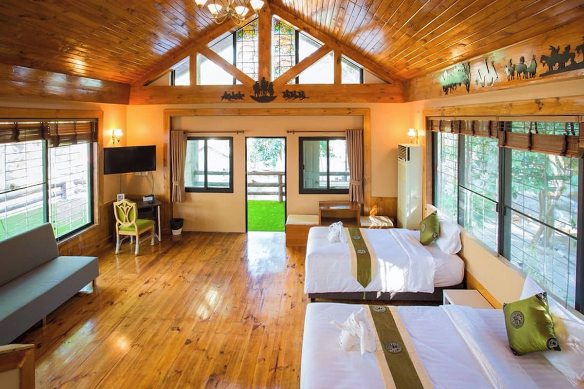 Habitación con piso de madera, dos camas, un sofá, un televisor y ventanas grandes.