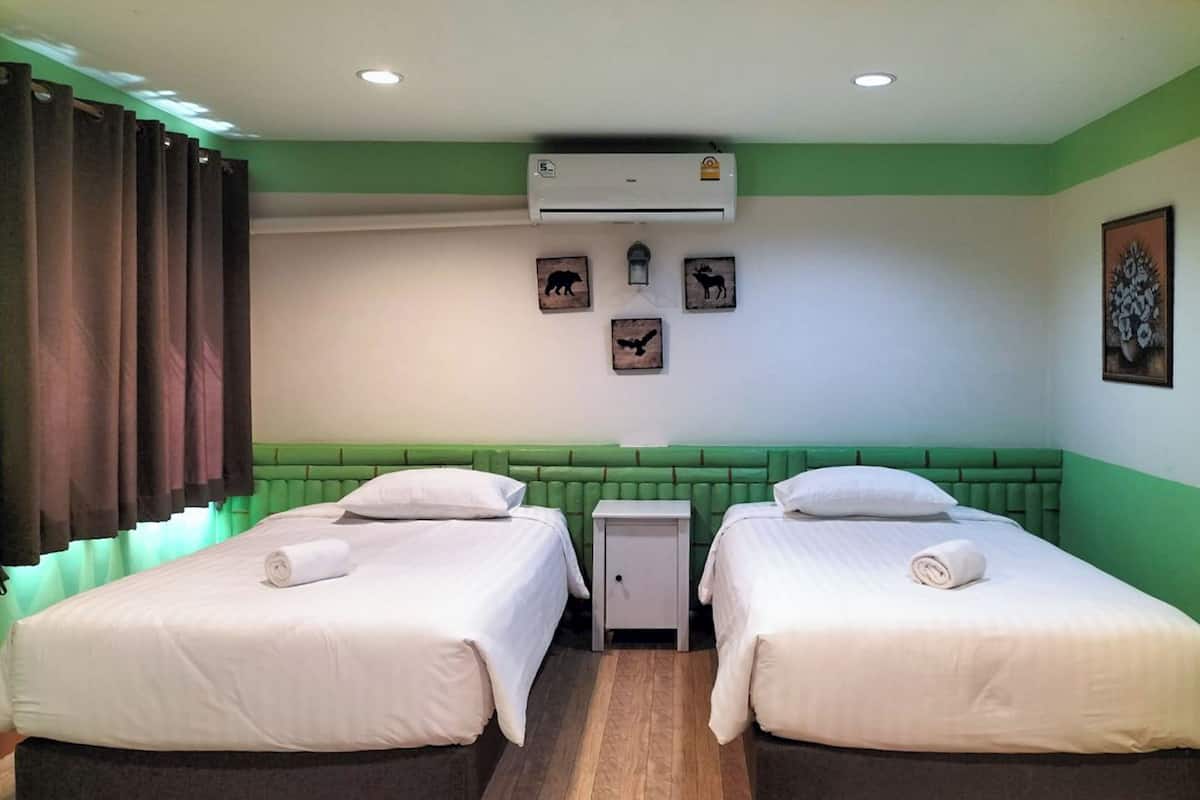 Una habitación con dos camas, una mesita de noche pequeña, un equipo de aire acondicionado y una pared con cuadros.