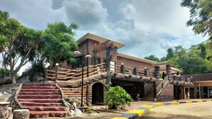 A rustic building with a wooden facade, a set of stairs leading to a covered entrance, and a paved area with yellow and black curbs. - Bhumisiri Hill Khaoyai (Pak Chong)