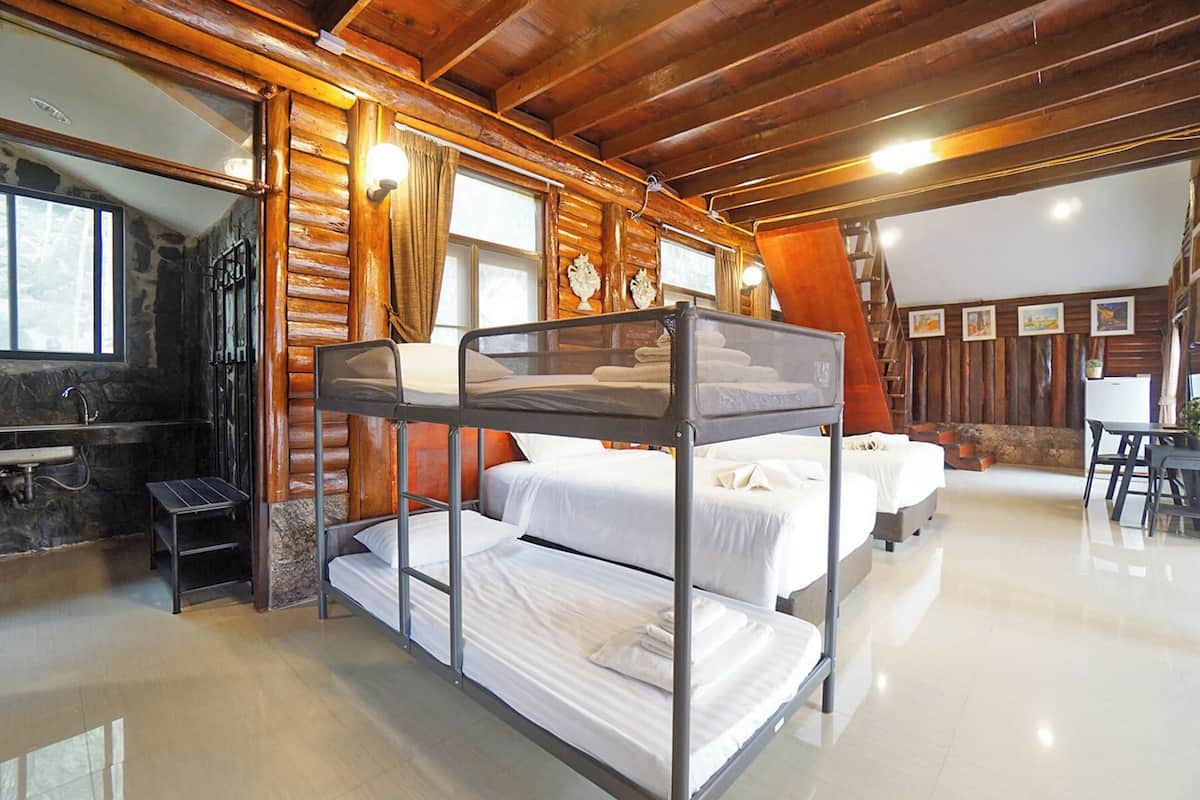 Habitación con literas, pared de piedra, techo de madera y una pequeña mesa.