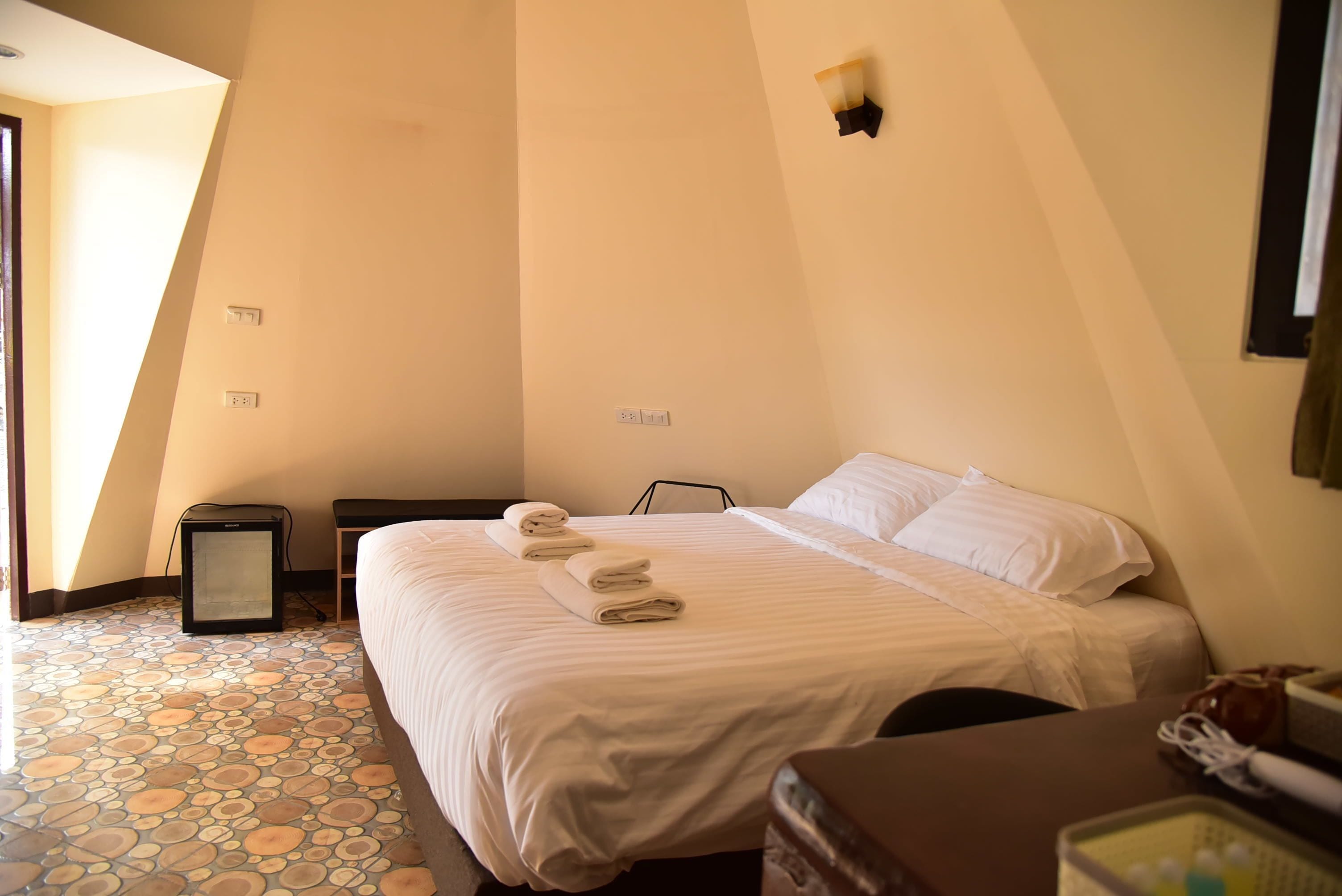 A bedroom with a bed, a bedside table, a lamp, and a tiled floor.