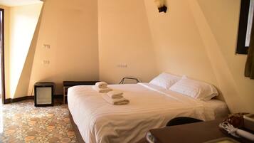 A bedroom with a bed, a bedside table, a lamp, and a tiled floor.
