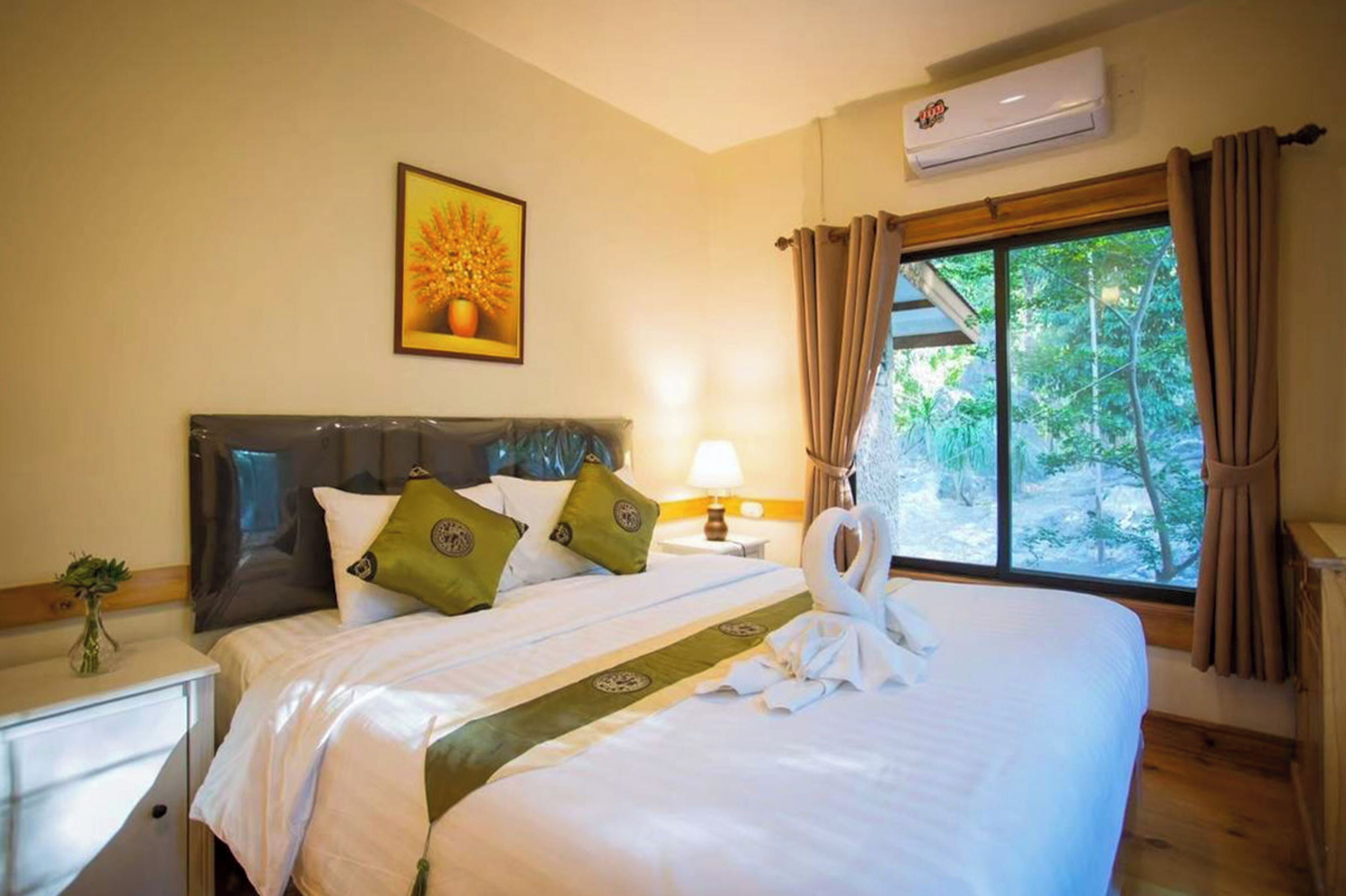 A hotel room with a bed, a nightstand, a lamp, a window with curtains, and an air conditioning unit.