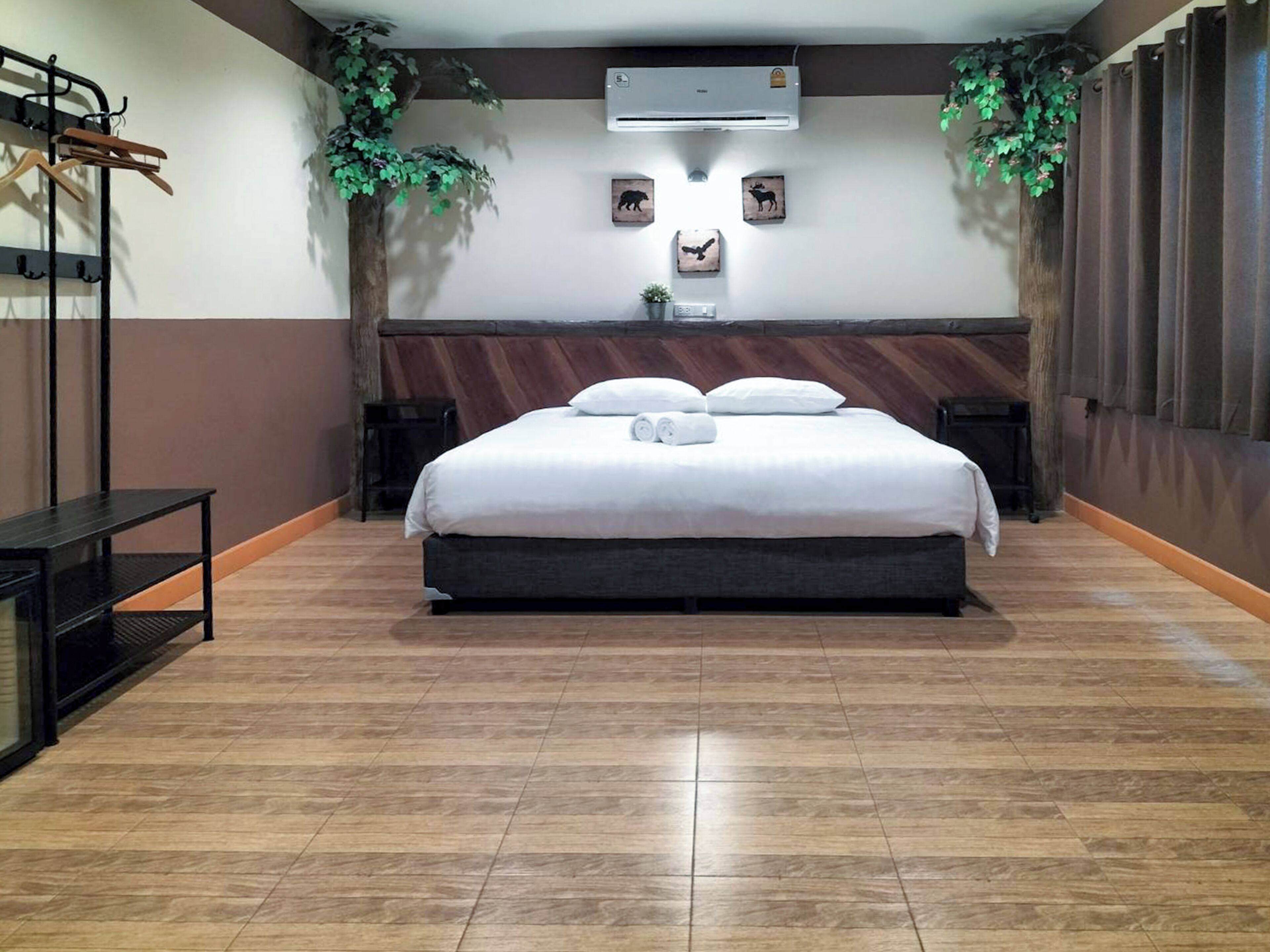 A neatly arranged hotel room with a large bed, a small bedside table, a wall-mounted air conditioner, and a potted plant.