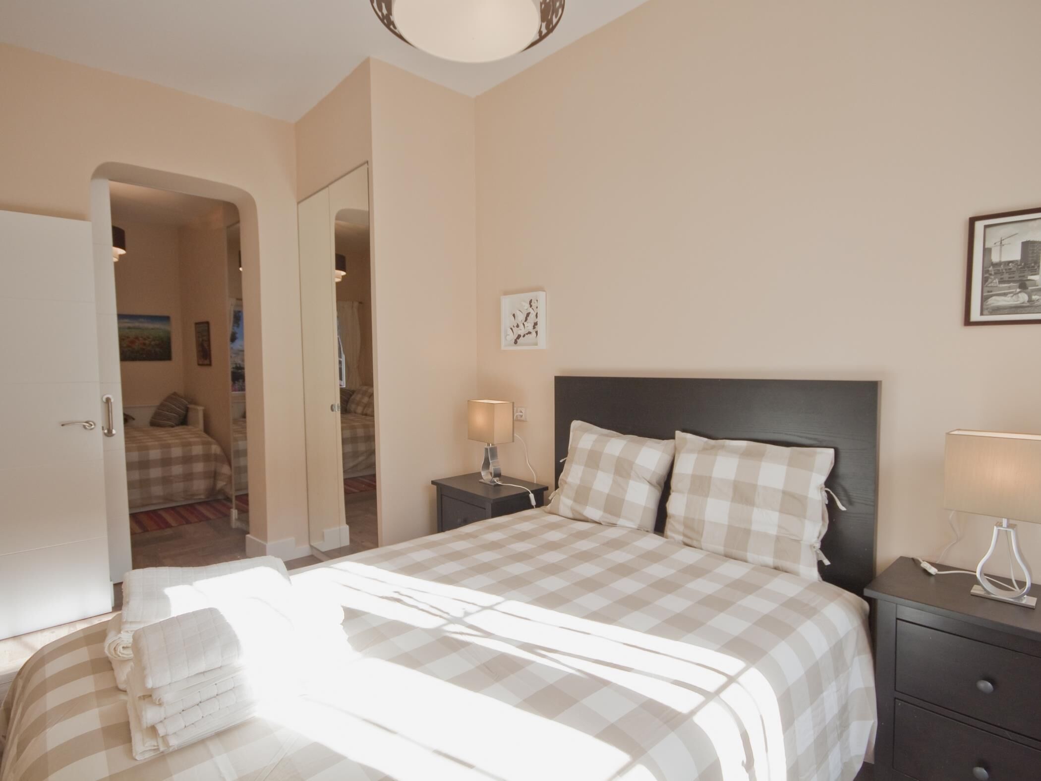 A bedroom with a large bed, a nightstand, a bedside lamp, and a door leading to another room.