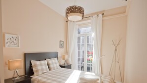 Une chambre à coucher bien rangée, avec une couvre-lit à carreaux, une lampe de chevet, une table de chevet, une fenêtre avec des rideaux et une lampe sur pied.