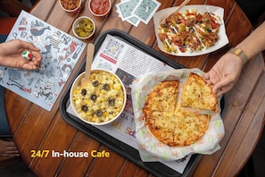 A dining table with various dishes, a QR code, and a person holding a slice of pizza. - goSTOPS Lite Jaipur (Jaipur)