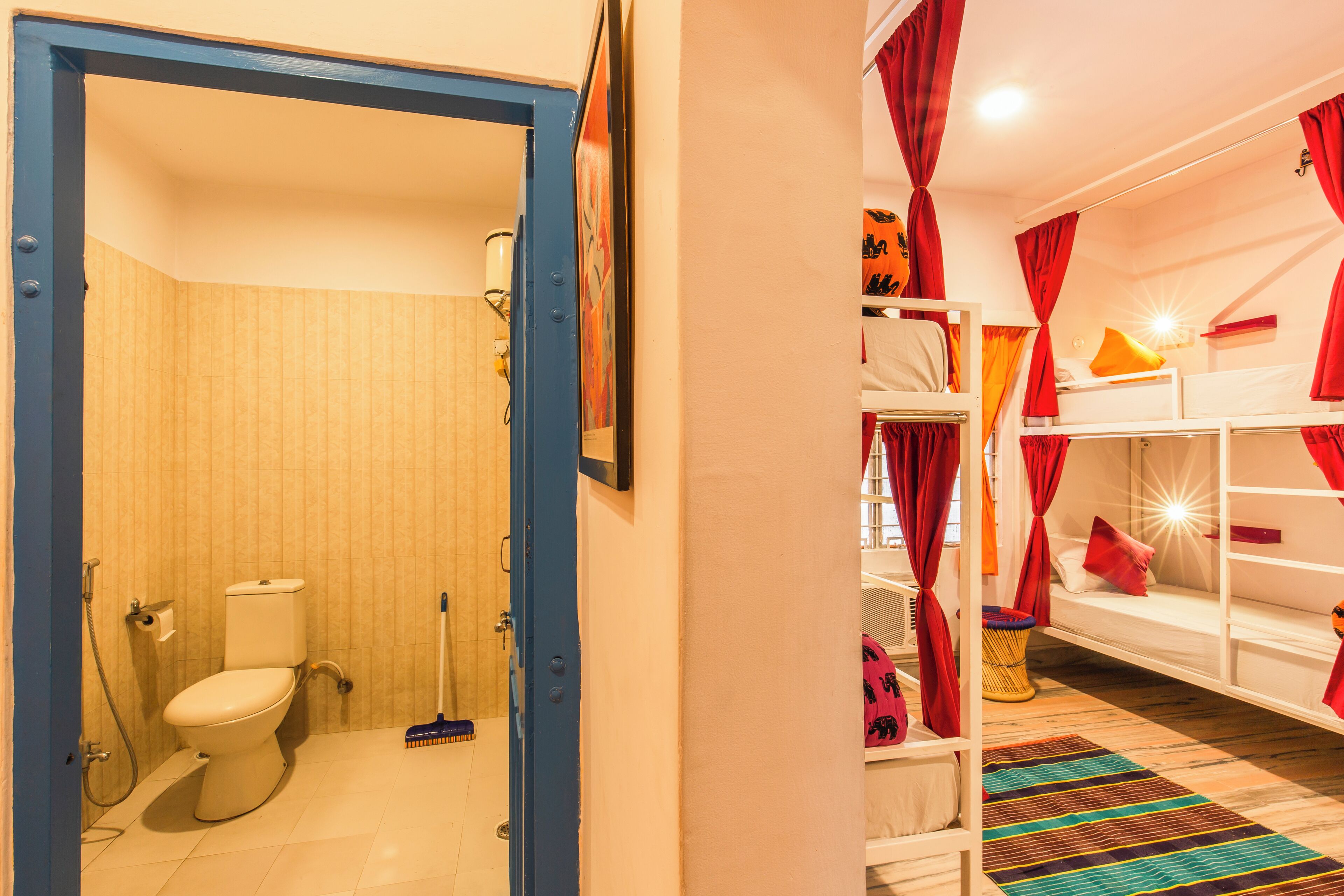 Un baño con inodoro y ducha, una cama con cortinas rojas, y una alfombra colorida.