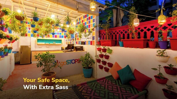 Een helder verlicht buitenterras met kleurrijke potplanten en een bord waarop staat: 'Your Safe Space, With Extra Sass'.
