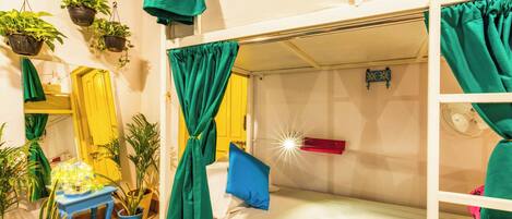 A bunk bed room with green curtains, a fan, and potted plants.