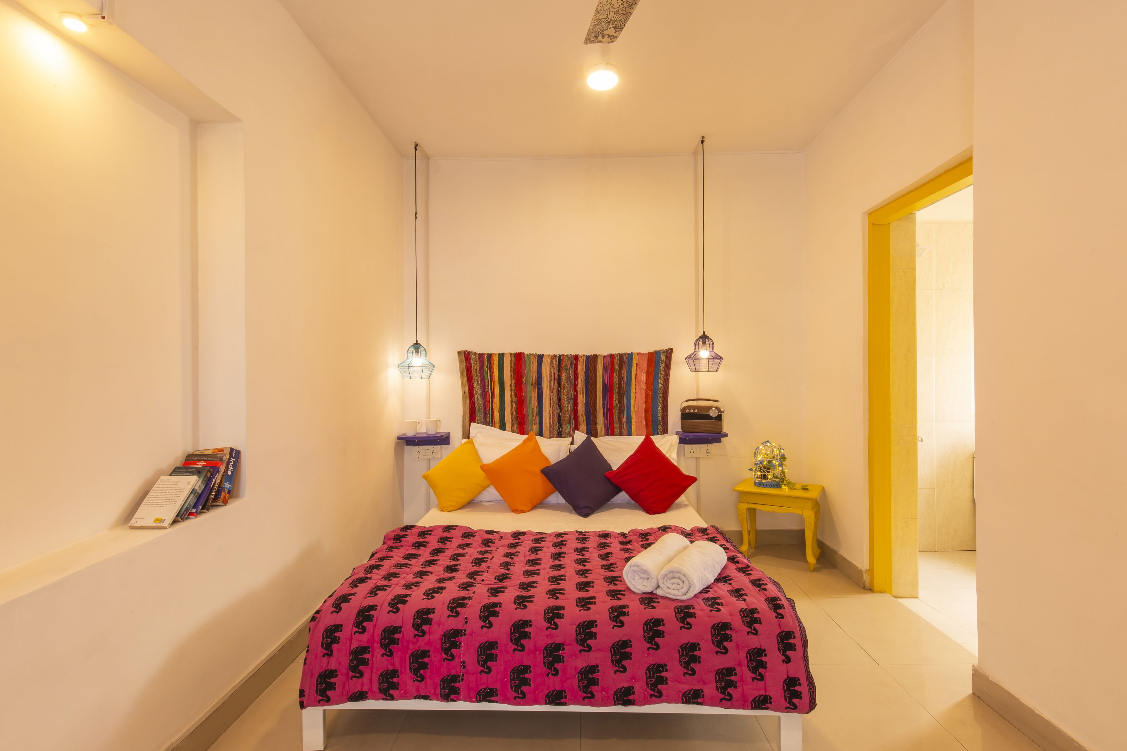 Une chambre bien rangée, avec un lit, des oreillers, une table de chevet et un luminaire suspendu.