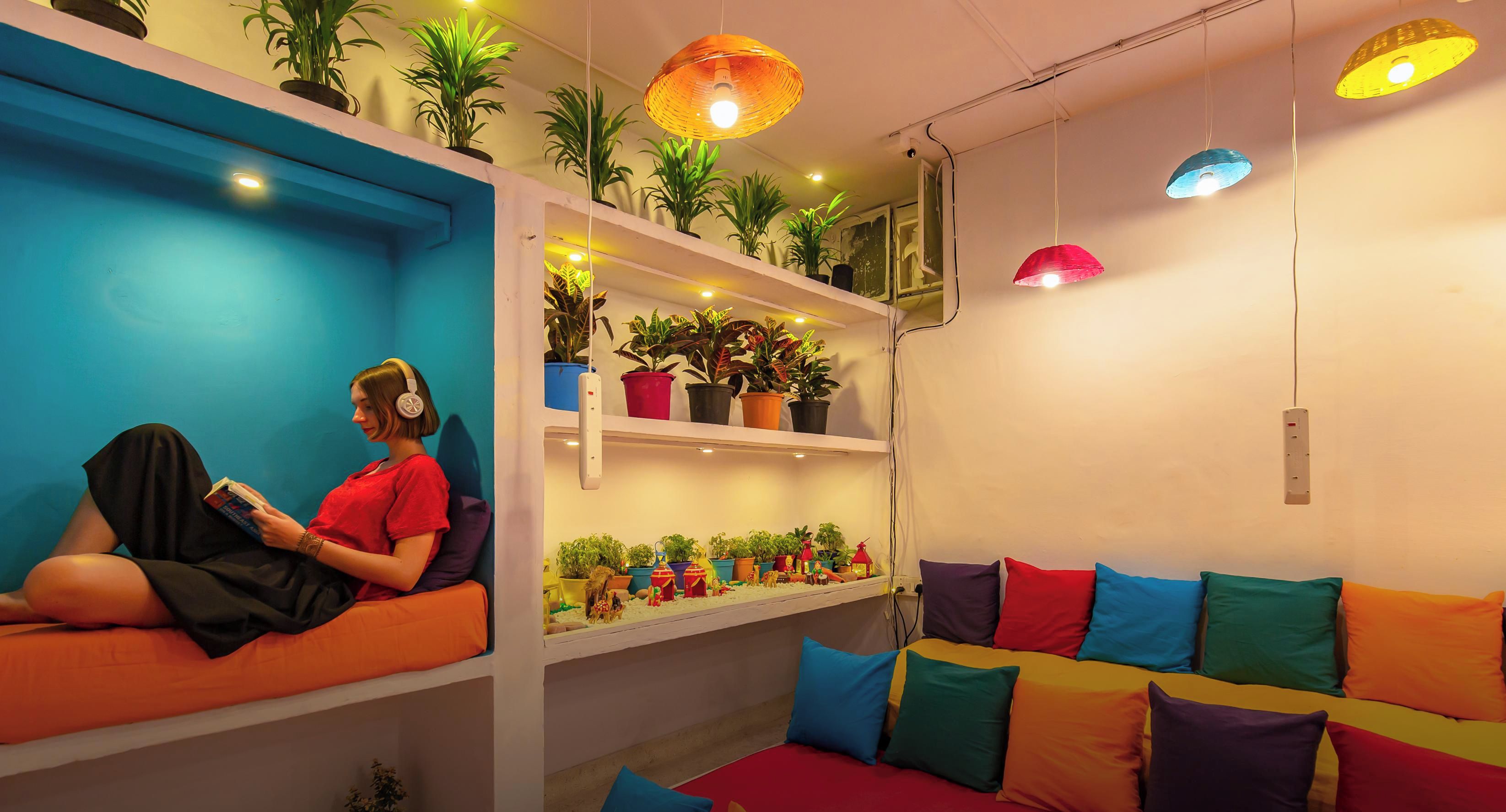 A cozy room with a bed, a reading area, and shelves with plants.