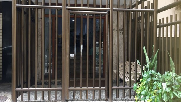 A metal gate with vertical bars, a potted plant, and a concrete bench. - Apartamento Copacabana Central (Rio de Janeiro)