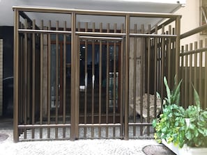 A metal gate with vertical bars, a potted plant, and a concrete bench. - Apartamento Copacabana Central (Rio de Janeiro)