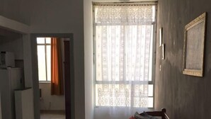A room with a bed, a window with curtains, a door, and a kitchenette area. - Apartamento Copacabana Central (Rio de Janeiro)