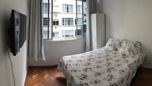 A bedroom with a bed, a TV, a window with curtains, and a view of buildings outside. - Apartamento Copacabana Central (Rio de Janeiro)