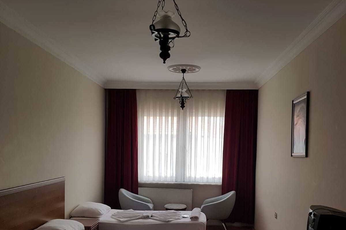 A hotel room with two beds, a sitting area with a chair and a table, a television, and a large window with curtains.