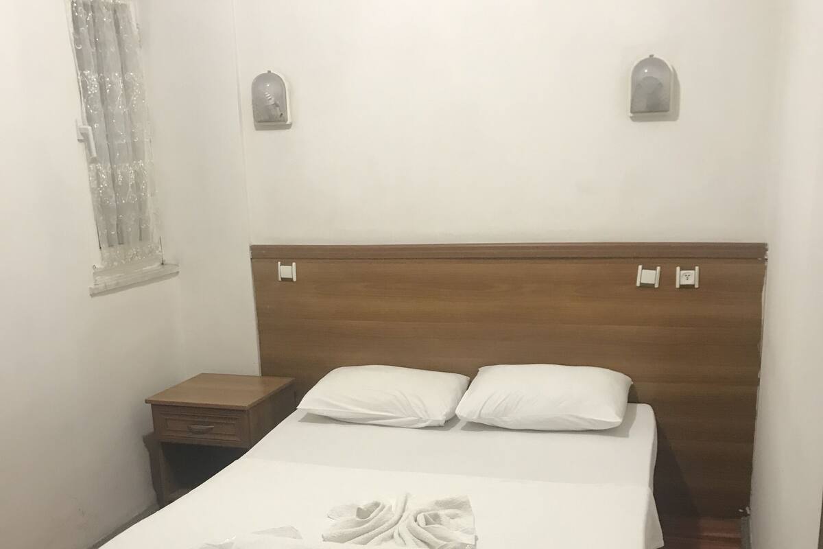 A neatly made bed with a wooden headboard, a nightstand, and a window with a curtain.