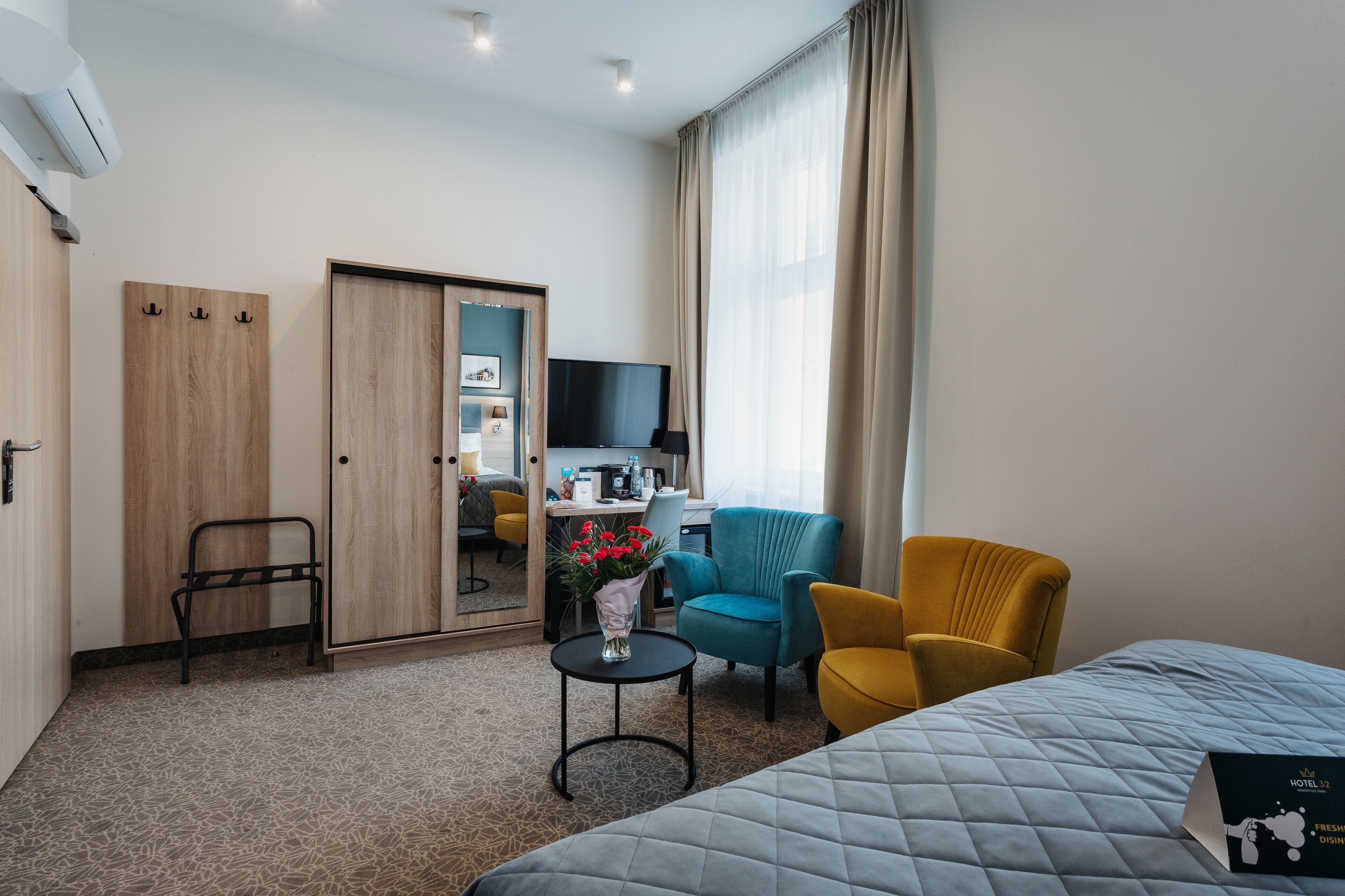 A hotel room with a bed, a desk, a TV, a chair, and a small table with a vase of flowers.