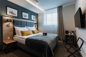 Habitación de hotel con cama, lámparas de noche, televisión, minibar y ventana con cortinas.