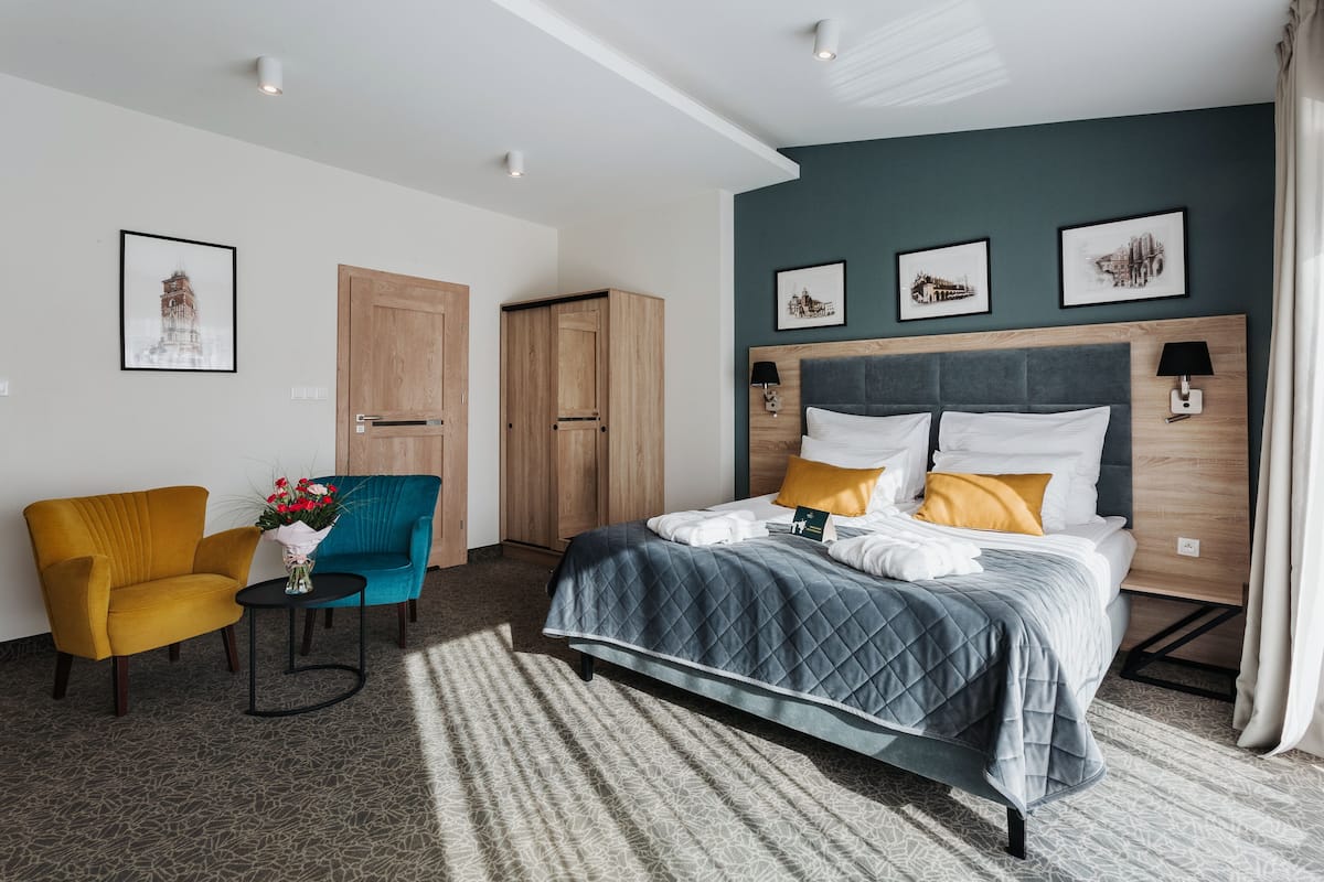 Une chambre d’hôtel avec un lit, deux chaises, une petite table ornée de fleurs et des œuvres d’art accrochées aux murs.