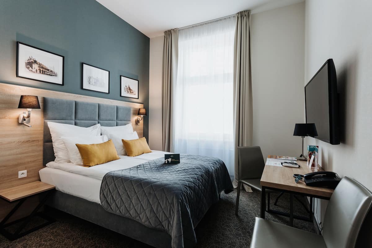 Une chambre d’hôtel avec un lit, un bureau, une chaise, une télévision et des tableaux encadrés au mur.