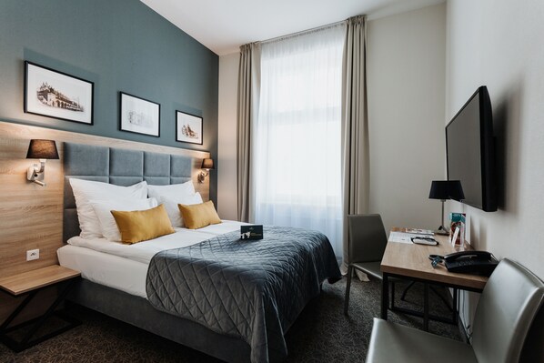 Une chambre d’hôtel avec un lit, un bureau, une chaise, une télévision et des tableaux encadrés au mur.