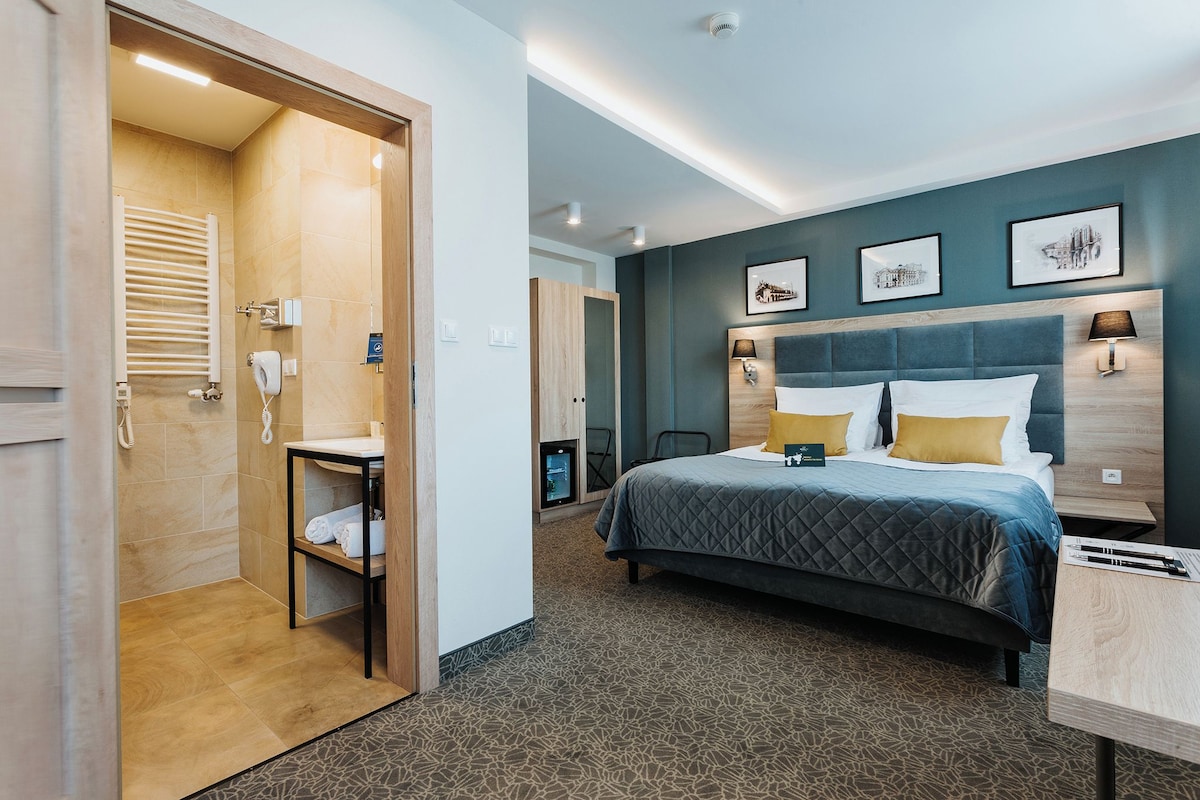 Una habitación de hotel con cama, mesitas de noche, escritorio, baño con ducha e inodoro.