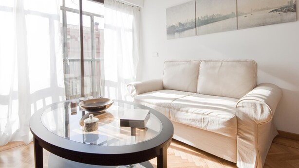 Een moderne woonkamer met een glazen salontafel, een beige bank en een stadsgezicht schilderij aan de muur.