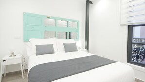 Un dormitorio con cama, mesita de noche, ventana con persianas e iluminación en la pared.