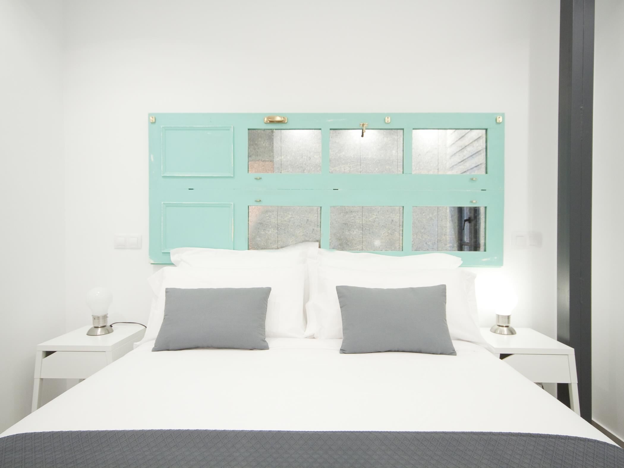 Een bed met een witte matras en twee kussens, aan weerszijden omringd door witte nachtkastjes met lampen.