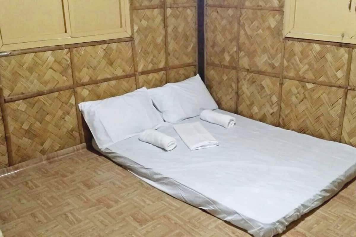 A single bed with white linens, a wooden floor, and a herringbone-patterned wall.