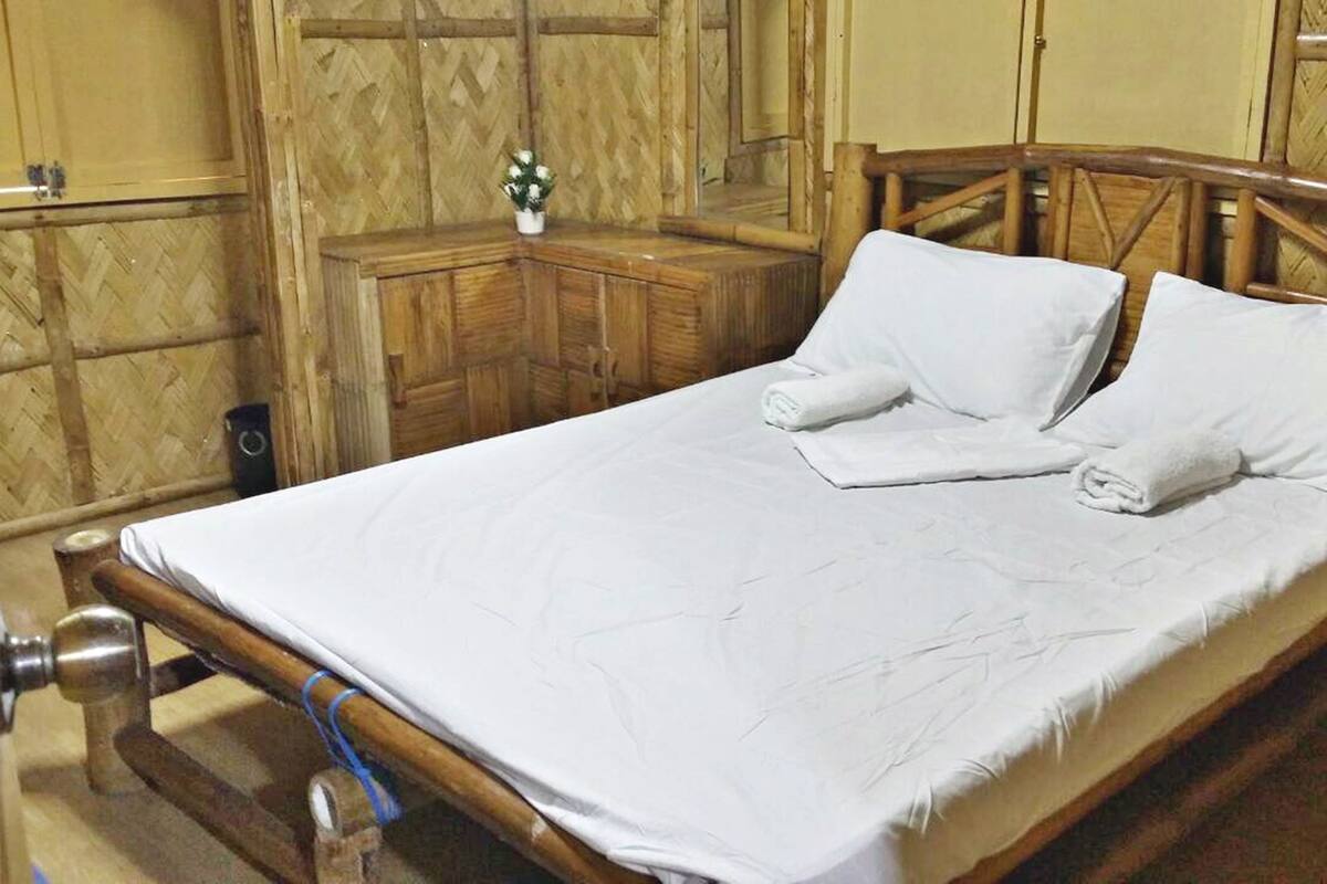 A bed with white linens, a wooden headboard, and a small bedside table with a vase of flowers.