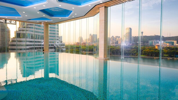 A modern indoor swimming pool with a cityscape view, large glass windows, and a unique ceiling design. - Lakeside Hotel Xiamen Airline (Xiamen)