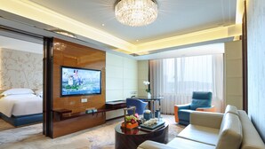 A hotel room with a bed, a TV, a seating area with a sofa and chairs, a coffee table with fruit, and a chandelier. - Lakeside Hotel Xiamen Airline (Xiamen)