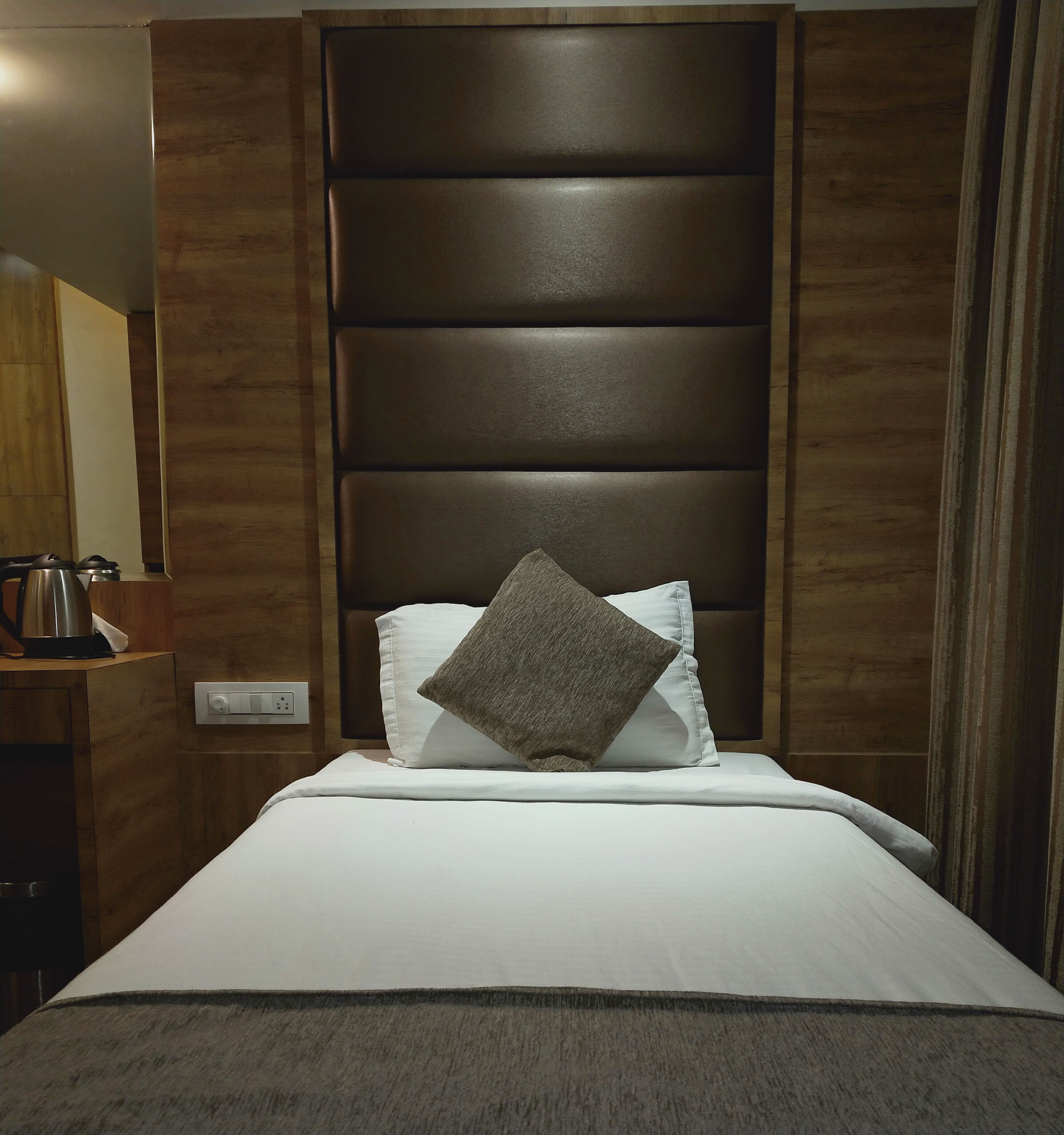 Une chambre d’hôtel comprenant un lit, une tête de lit, une table de chevet avec une bouilloire et une prise électrique.