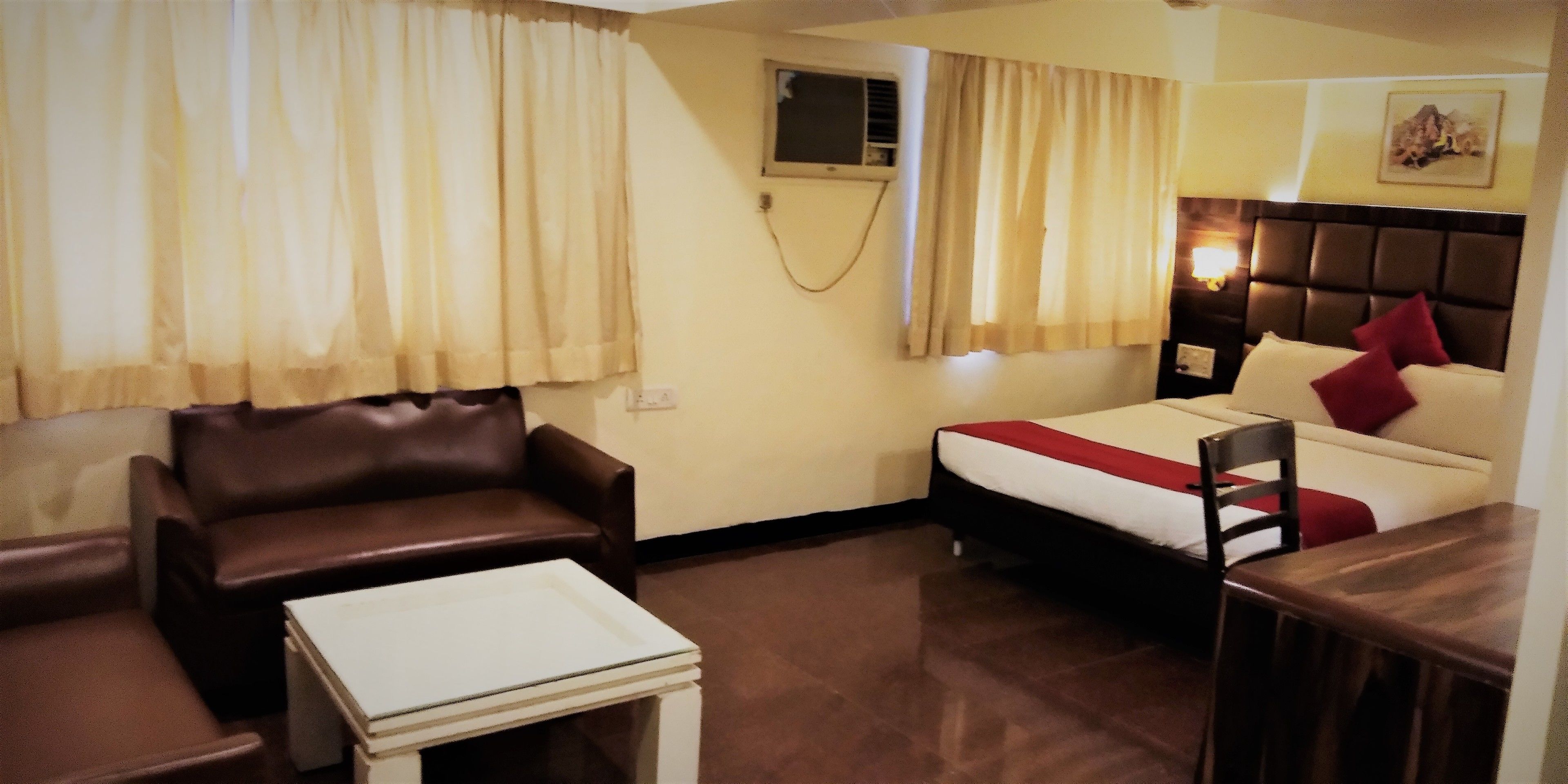 A hotel room with a bed, a sofa, a small table, and a window with curtains.