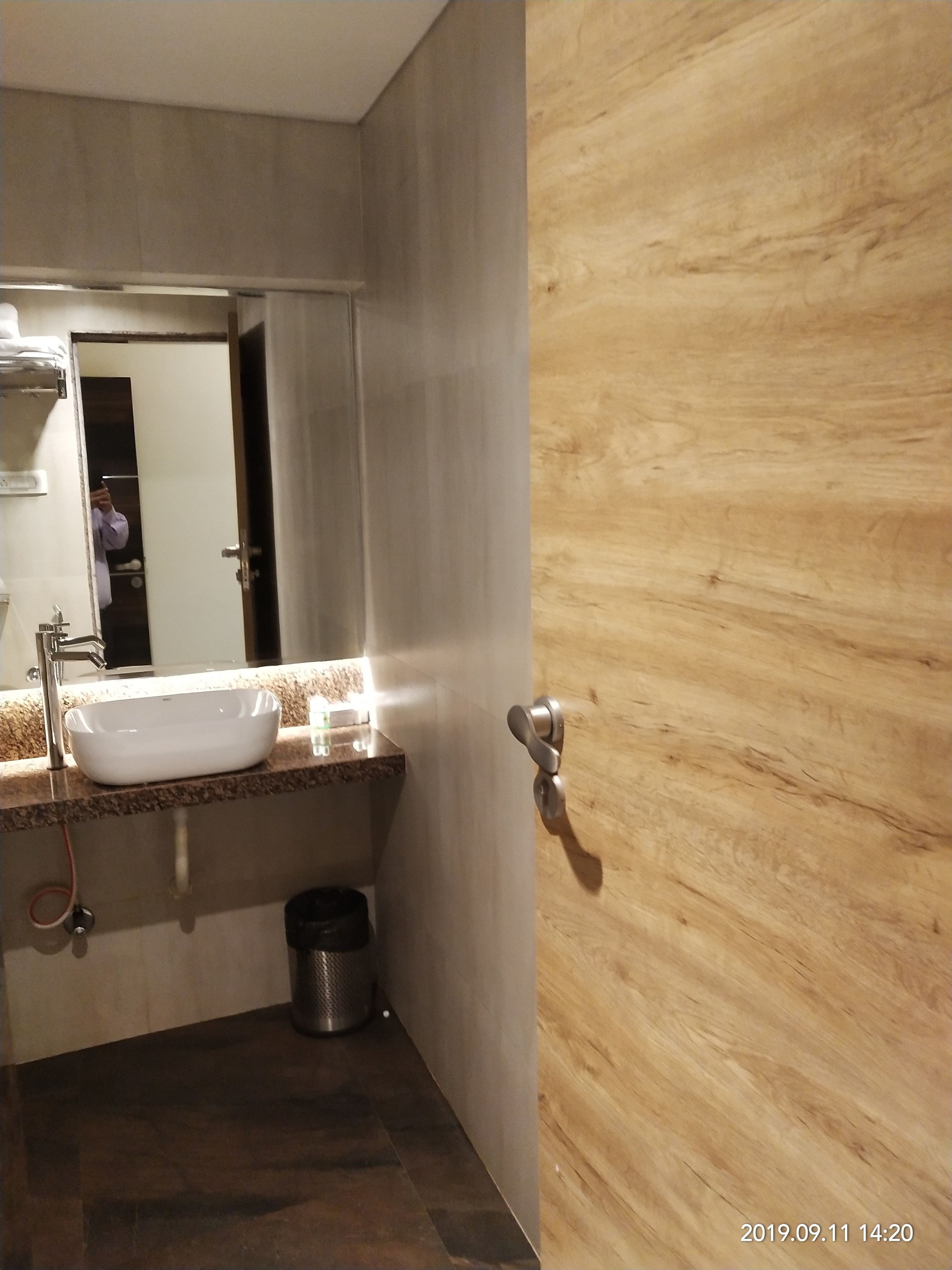 Un baño moderno con un lavamanos blanco, un espejo y una puerta de madera.