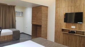 Quarto de hotel com uma cama, televisão presa a uma parede de madeira, um pequeno estante e uma janela com cortinas.