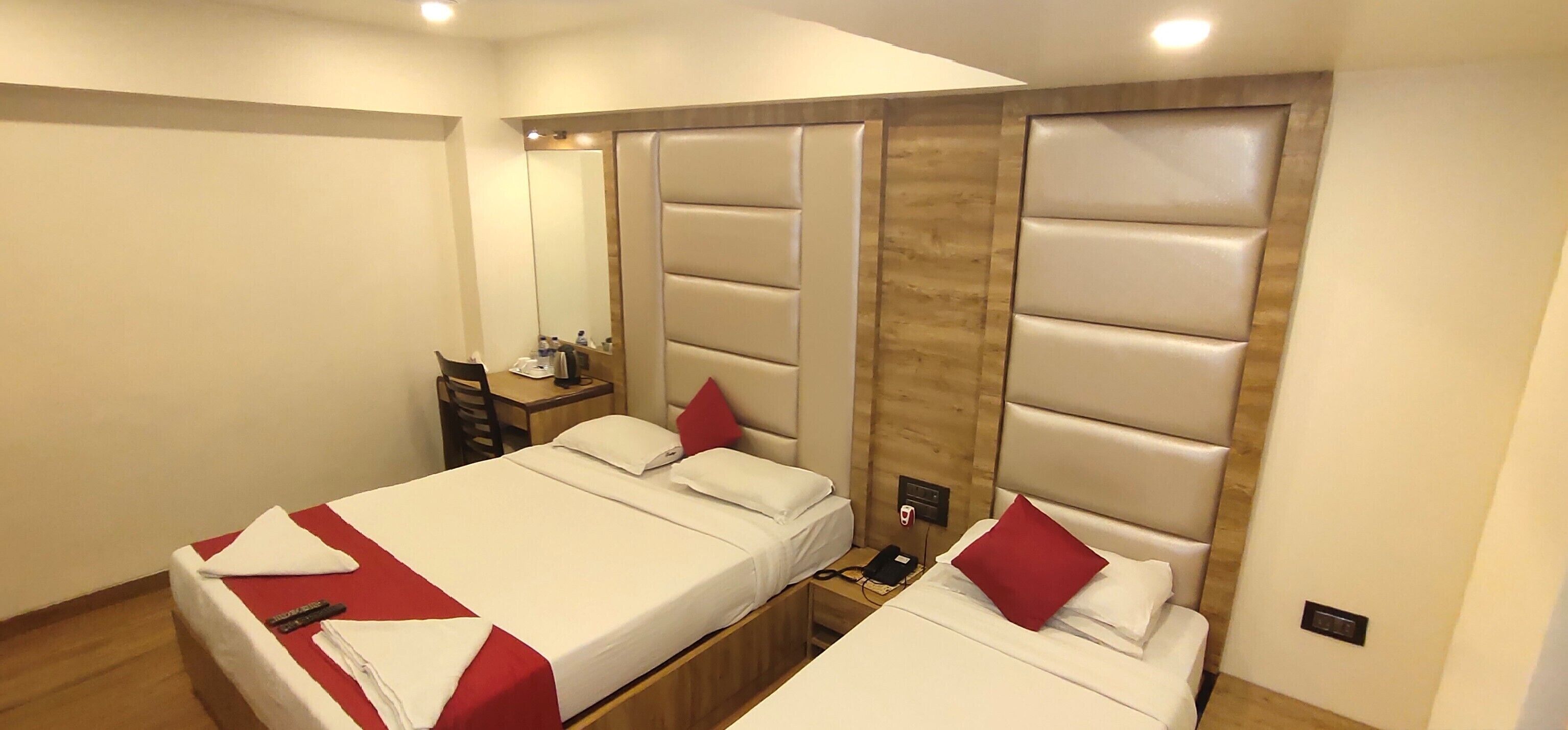 A hotel room with two beds, a wooden headboard, a nightstand, a mirror, and a small table with a lamp.