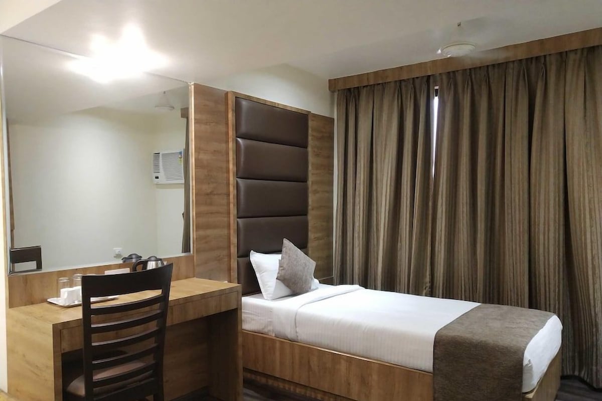 Ein Hotelzimmer mit einem Bett, einem Schreibtisch, einem Stuhl, einem großen Spiegel und einem Fenster mit Vorhängen.