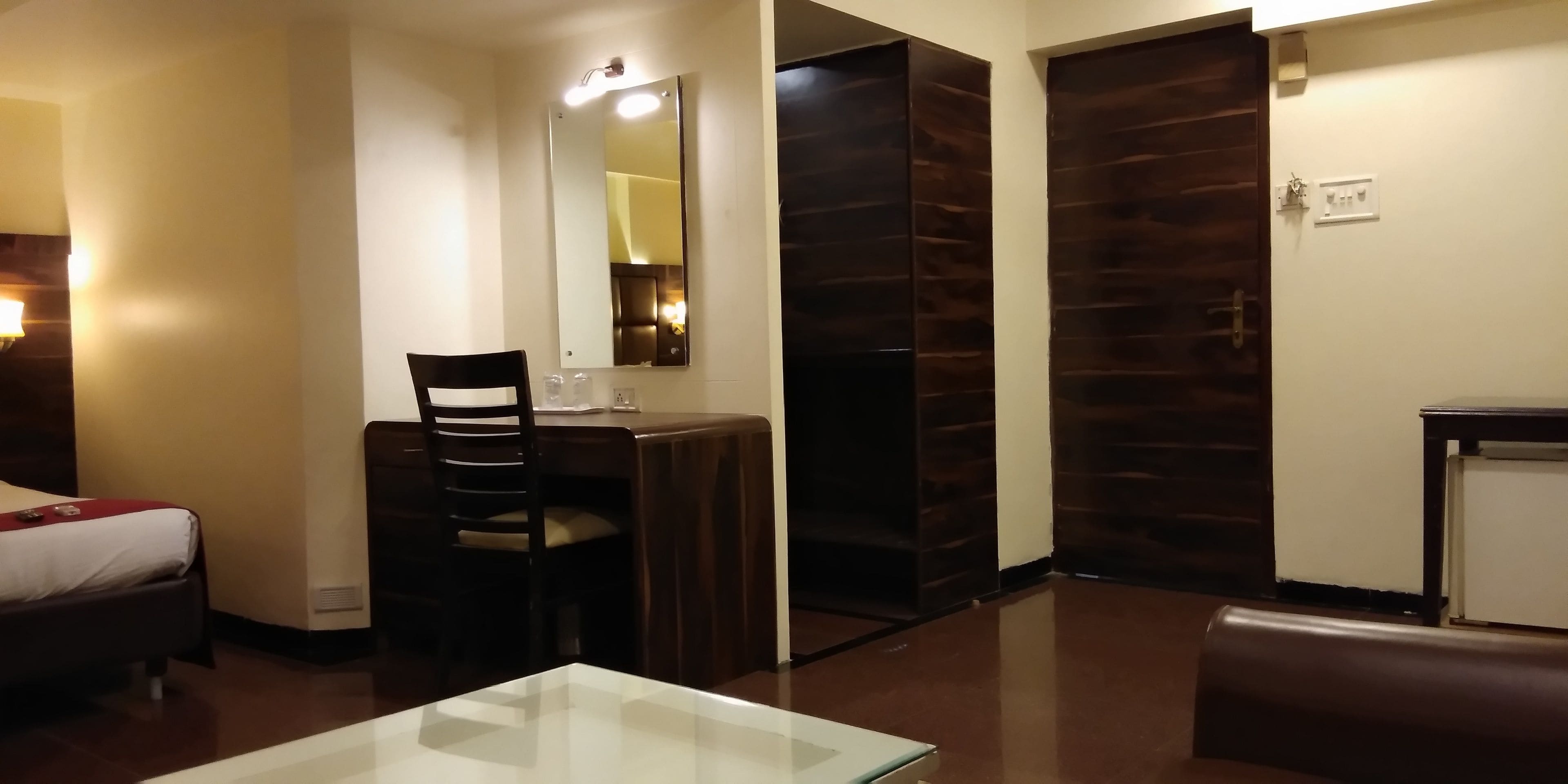 A hotel room with a bed, a desk with a chair, a mirror, and a wardrobe.