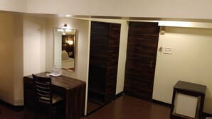 Quarto de hotel com uma escrivaninha de madeira, uma cadeira, uma mesinha, uma televisão e um espelho.