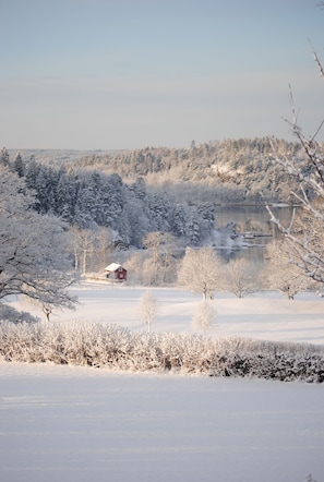A snow-covered landscape with a red barn and a lake in the background. - Anfasteröd Gårdsvik (Ljungskile)