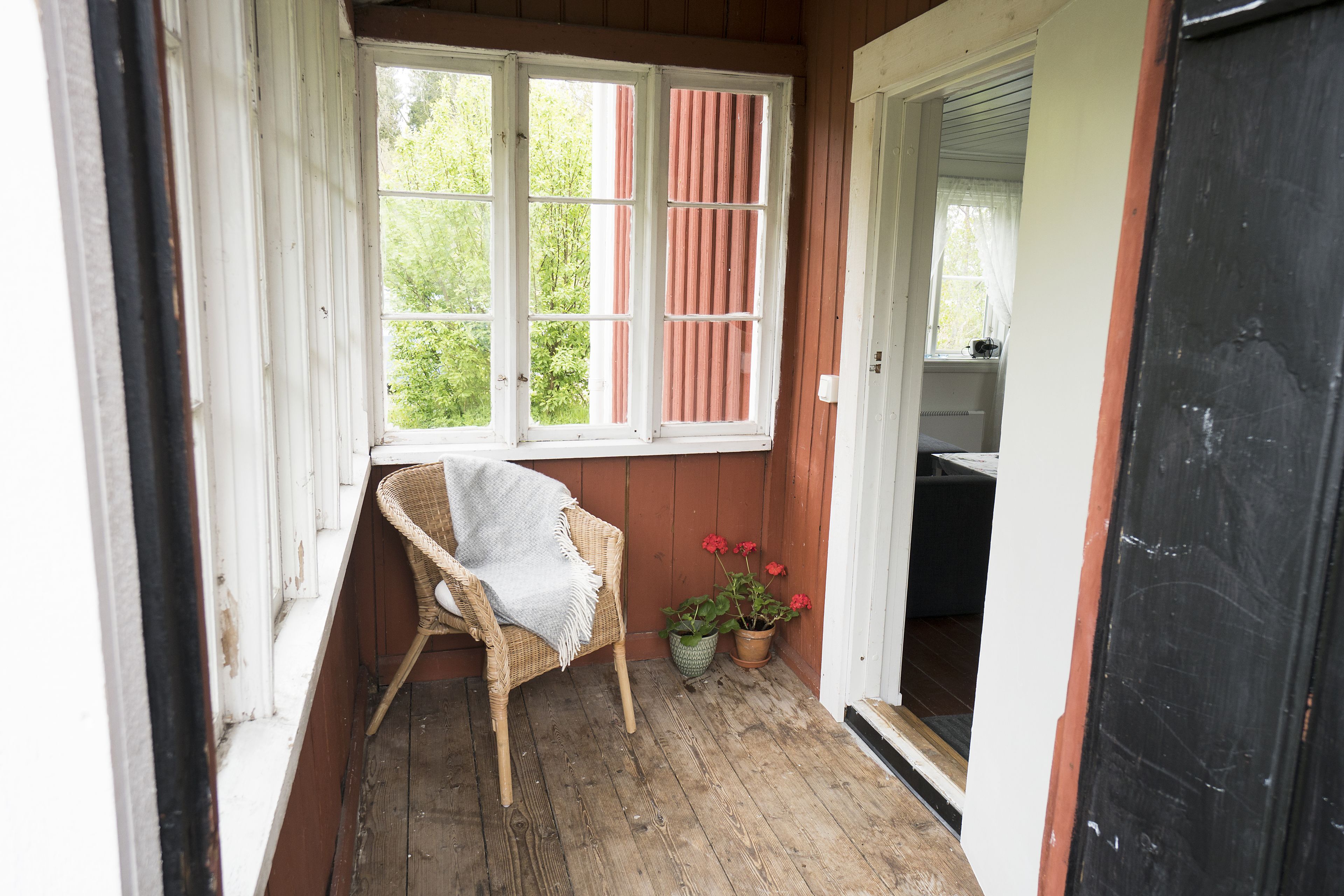 A wooden porch with a wicker chair and potted plants.