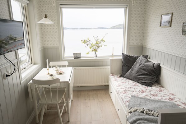 A cozy room with a white table, a white chair, a bed with floral bedding, and a window with a view of a lake. - Anfasteröd Gårdsvik (Ljungskile)
