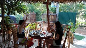 An outdoor dining area with a thatched roof, wooden chairs, and a table set for two.