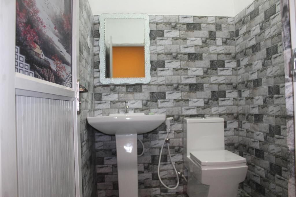 A bathroom with a white sink, toilet, and a mirror with a decorative frame. The walls are covered with patterned tiles.