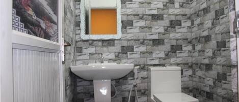 A bathroom with a white sink, toilet, and a mirror with a decorative frame. The walls are covered with patterned tiles.